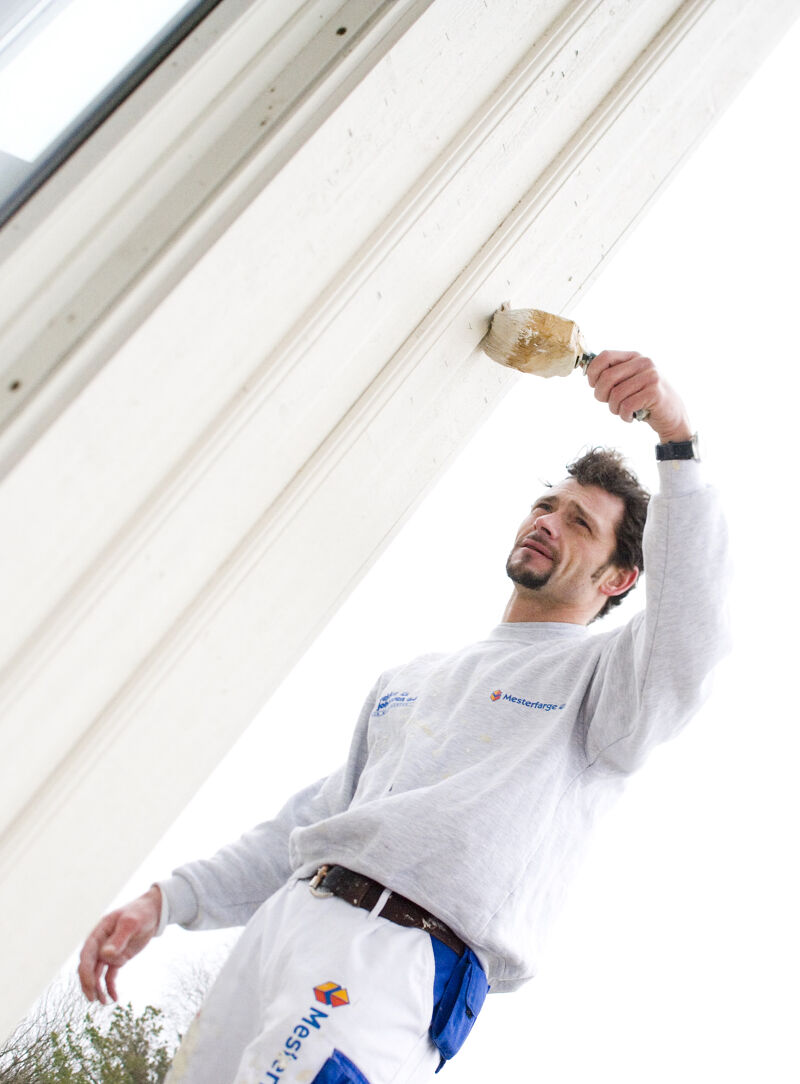 Maler setter et strøk hvitmaling på et hus